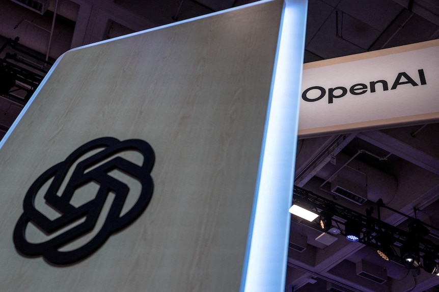 An upward-shot photo shows large wall with the OpenAI logo, behind it a banner reads 'OpenAI'